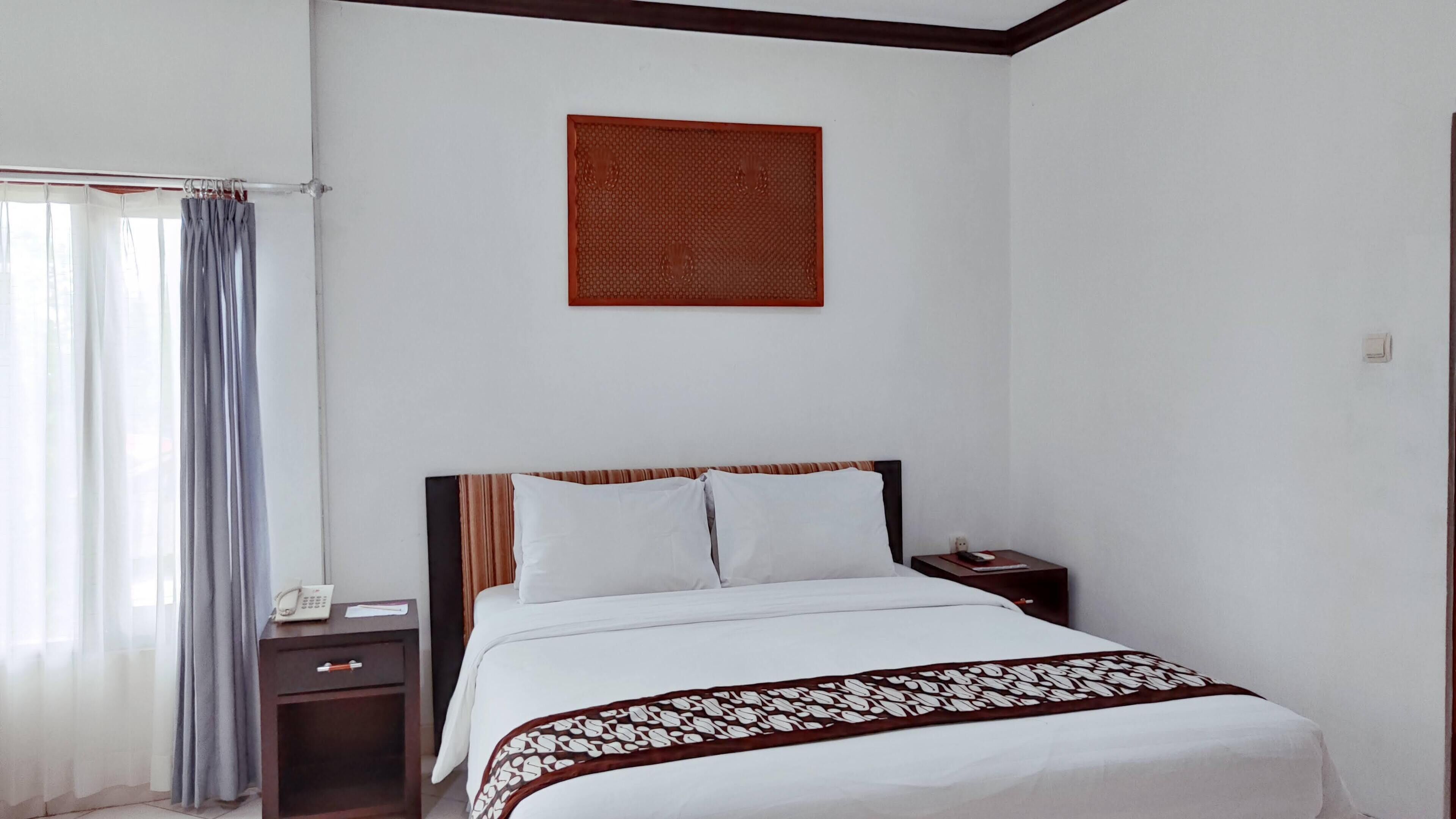 A hotel room with a bed, a nightstand, a telephone, and a wall-mounted artwork.