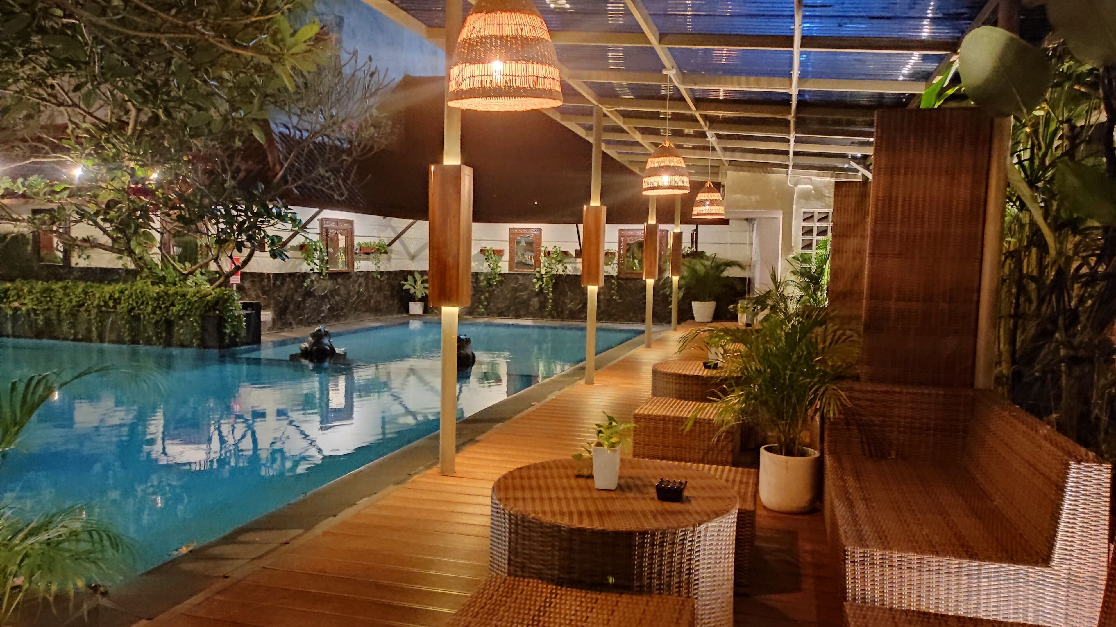 An indoor pool area with wooden flooring, wicker furniture, and hanging lights.