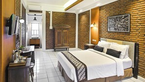 Una habitación de hotel moderna con pared de ladrillo, una cama grande con ropa de cama blanca, un armario de madera, un escritorio con una silla y un baño pequeño.