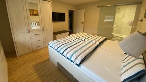 A bedroom with a bed, a wardrobe, a desk, and a shower area.
