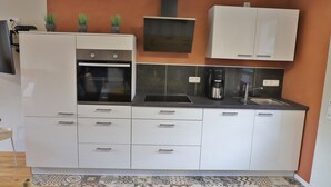 A modern kitchen with white cabinets, a built-in oven, a coffee maker, and a sink.