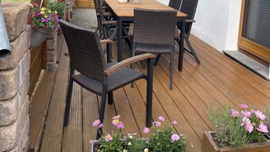 An outdoor patio with a wooden table and chairs, surrounded by stone walls and potted plants.