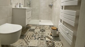 A bathroom with a shower, toilet, sink, and patterned tiles.
