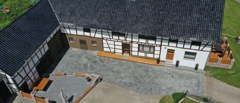 A traditional half-timbered building with a tiled roof, a paved courtyard, and a wooden deck with outdoor furniture.