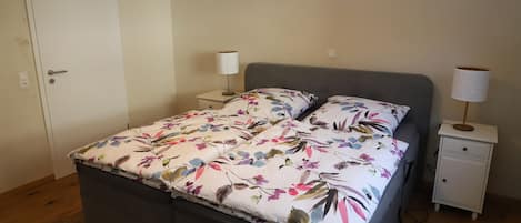 A bedroom with a bed, two bedside tables, a nightstand, a door, and a wall socket.