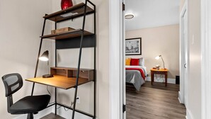 Ein gemütlicher Raum mit Schreibtisch, Stuhl und einem Bett mit roter und grauer Tagesdecke.
