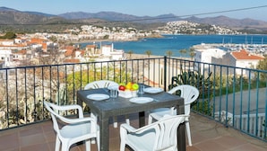 Ein Balkon mit Tisch für zwei Personen, Blick auf eine Küstenstadt und das Meer.