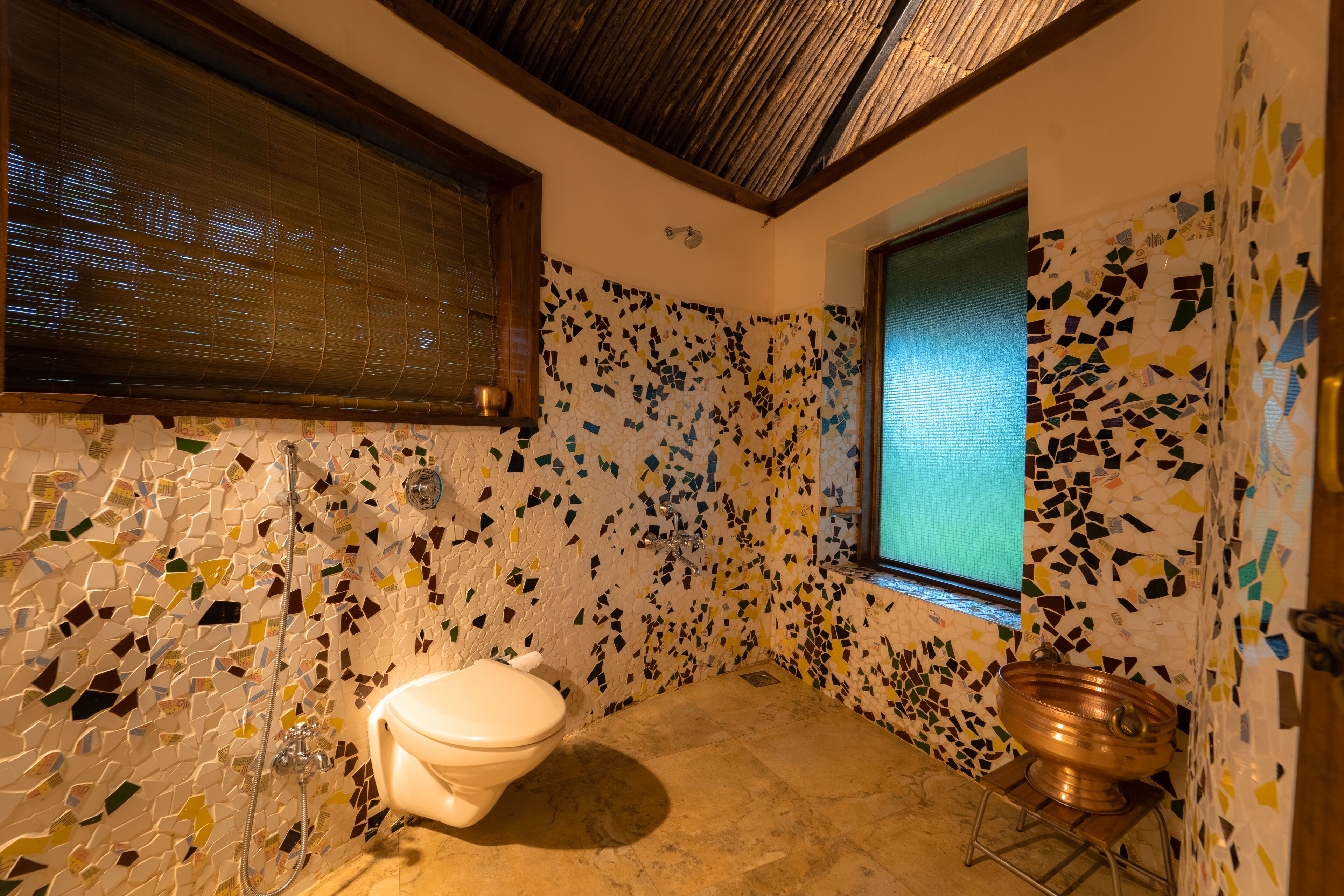 A bathroom with mosaic tile walls, a toilet, a shower, and a window.