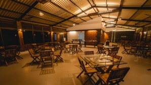 A spacious indoor dining area with high ceilings, wooden tables and chairs, and a brick accent wall. - Shatavari Eco Resort (Khanapur)