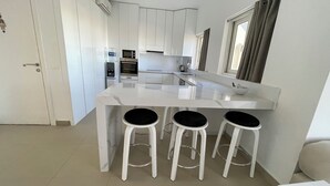 A modern kitchen with white cabinets, a marble countertop, and three black stools. - El-Gouna, Water Side, 3 room apartment, Sunny, Modern with pool, WaterSki view (El-Gouna)