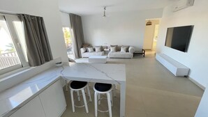 A modern living room with a sofa set, a TV, and a dining area with stools. - El-Gouna, Water Side, 3 room apartment, Sunny, Modern with pool, WaterSki view (El-Gouna)
