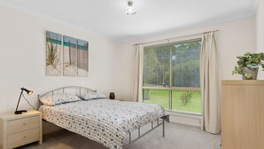 Een slaapkamer met een bed, nachtkastje, lamp en een raam met gordijnen.