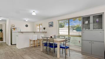 A modern kitchen with a dining area, featuring a wooden table, chairs, and a refrigerator.