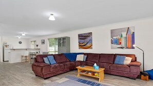 Een moderne woonkamer met een bruine hoekbank, een houten salontafel, en een eethoek met een keuken op de achtergrond.