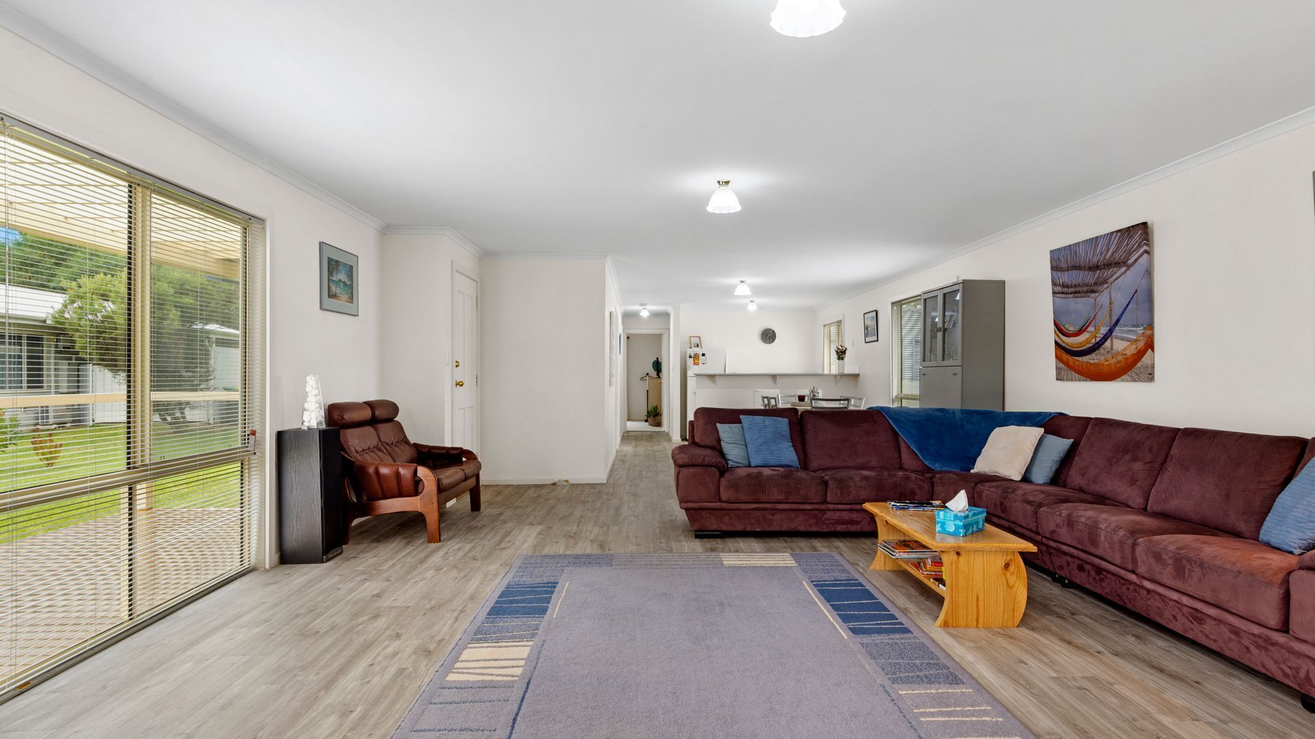 A spacious living room with a large sofa, a recliner, and a coffee table. There is a view through the glass door to the outside.