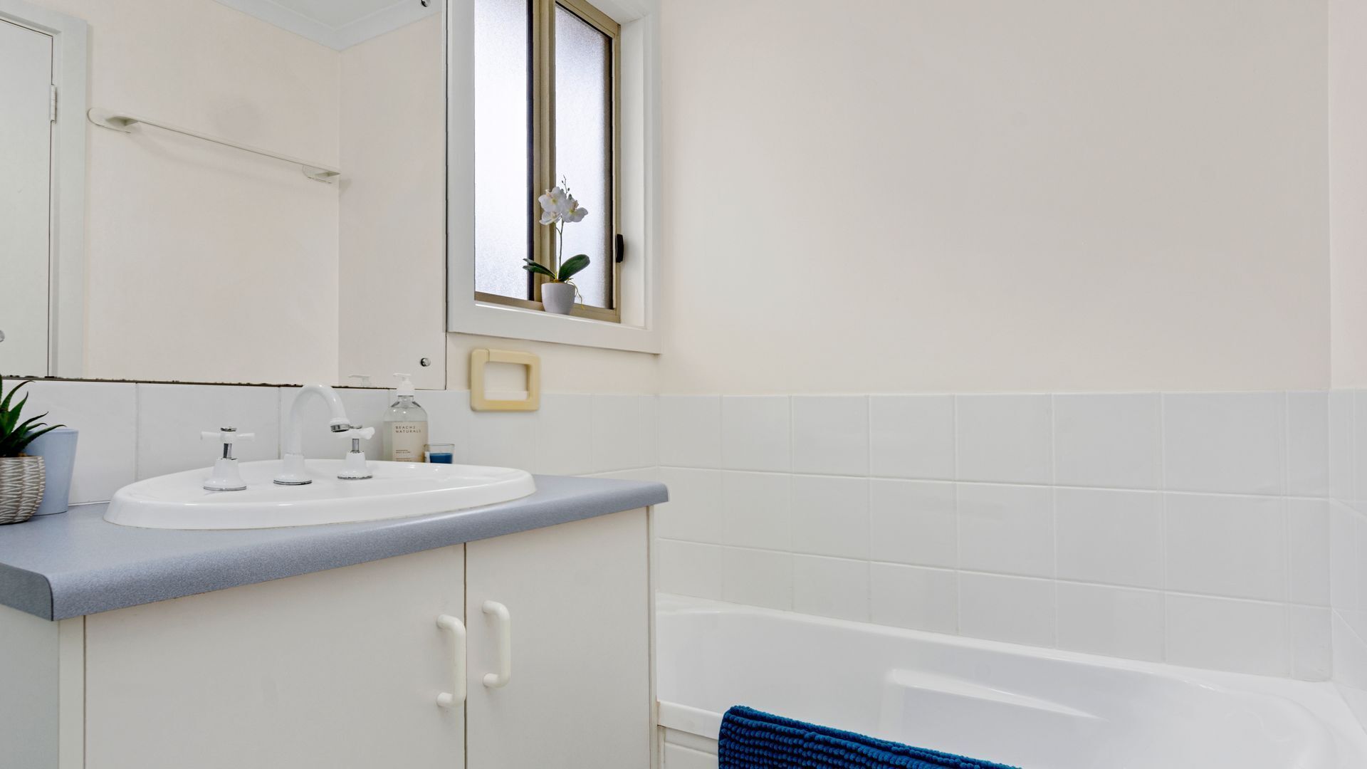 A bathroom with a white sink, a mirror, a window, and a bathtub.