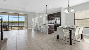A modern kitchen with a large island, bar stools, and a dining area with a view of the outdoors. - Beautiful 4 Bedroom Home With Pool Overlooking Lake Views (Haines city)
