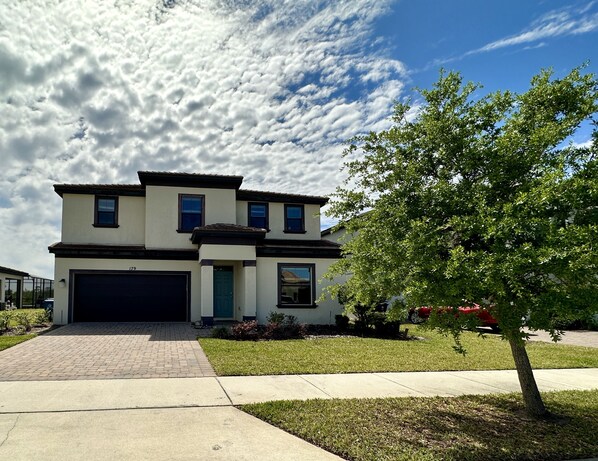 A two-story house with a garage, a driveway, and a tree in the front yard.