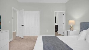 A bedroom with a bed, a nightstand, a lamp, and a door leading to another room. - Beautiful 4 Bedroom Home With Pool Overlooking Lake Views (Haines city)