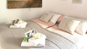 Une chambre à coucher avec un grand tableau représentant un coucher de soleil, un lit avec une literie rose et deux coussins ornés d’un motif de Bouddha.