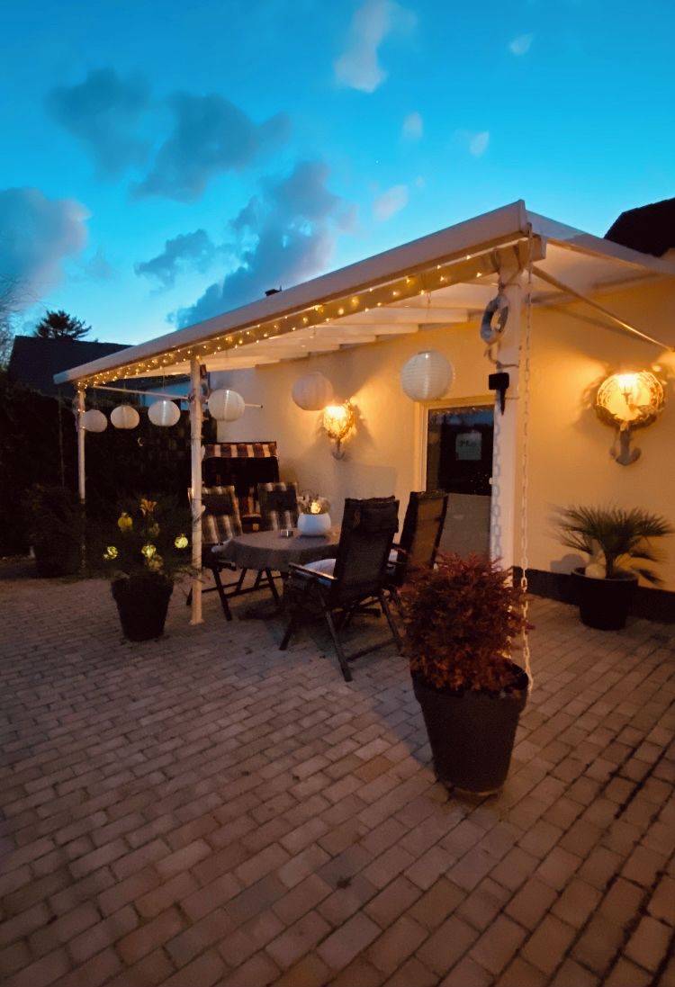 An outdoor patio area with a covered seating area, string lights, and potted plants.