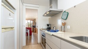 A modern kitchen with a stainless steel sink, a built-in oven, and a range hood. There is a red chair and a dining table visible in the background. - Apartment LLenaire in Puerto Pollensa by Home Villas 360 (Puerto Pollensa)