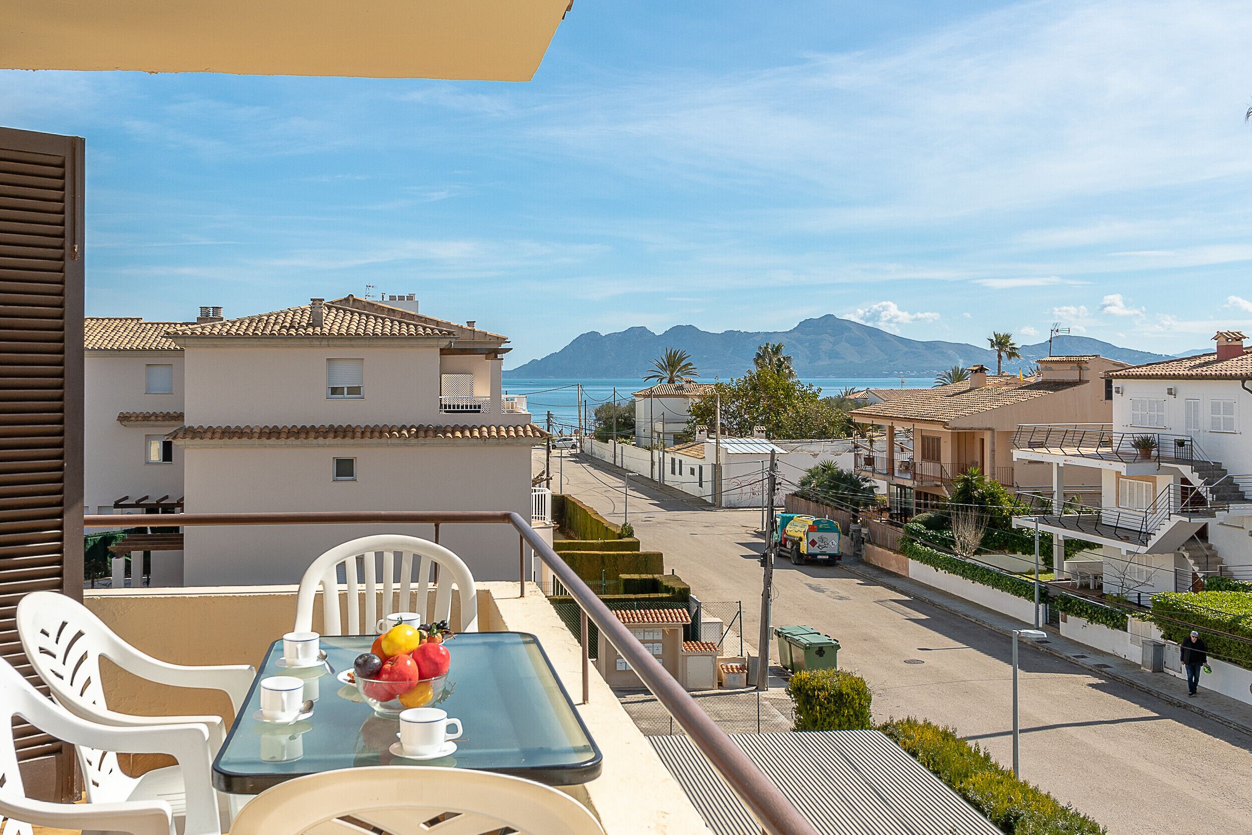 A balcony with a table set for two, overlooking a street with buildings and a mountain in the distance.