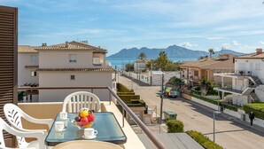A balcony with a table set for two, overlooking a street with buildings and a mountain in the distance. - Apartment LLenaire in Puerto Pollensa by Home Villas 360 (Puerto Pollensa)