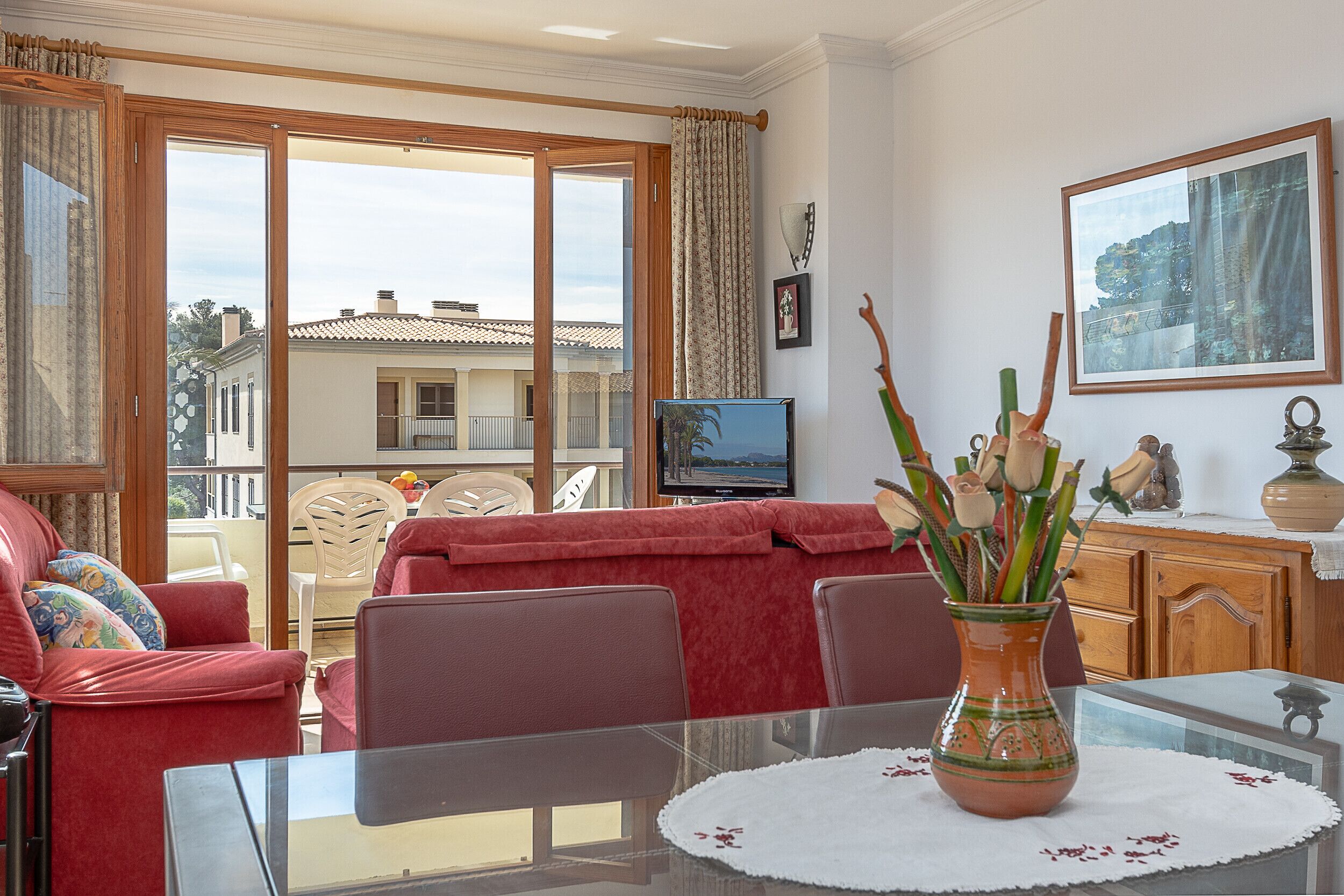 A living room with a glass table, red sofa, and a vase with flowers.