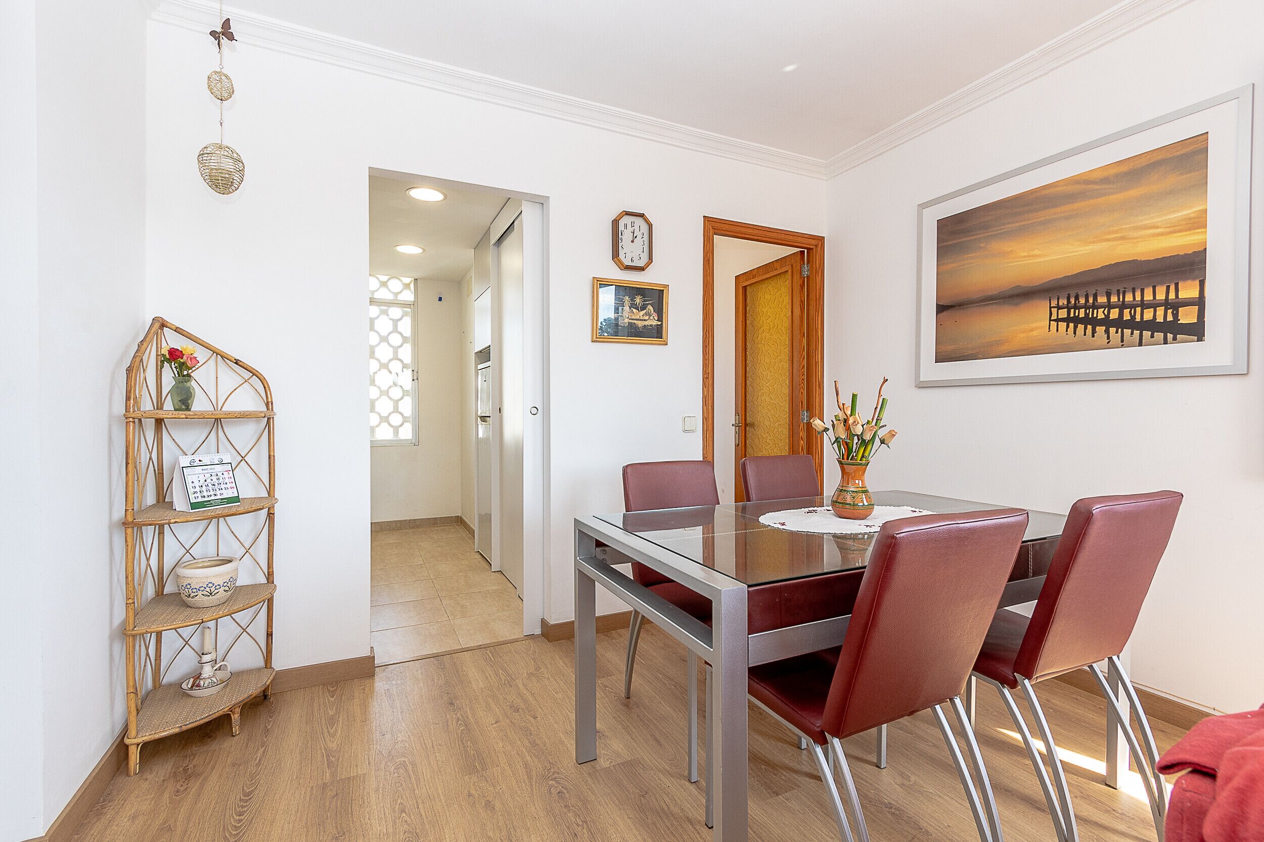 A dining area with a glass table, red chairs, a wooden sideboard, and a painting on the wall.
