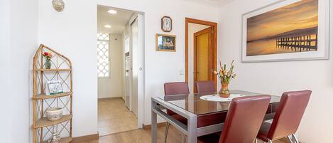 A dining area with a glass table, red chairs, a wooden sideboard, and a painting on the wall.