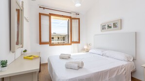 A bedroom with a bed, a desk, a chair, a window, and a bedside table with a lamp. - Apartment LLenaire in Puerto Pollensa by Home Villas 360 (Puerto Pollensa)