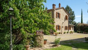 A stone house with a garden, a lamp post, and a paved driveway.