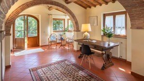 A spacious room with a tiled floor, a wooden table with chairs, a lamp, and a window with curtains.
