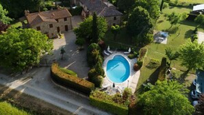An aerial view of a property with a swimming pool, stone buildings, and surrounding greenery.