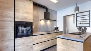 Une cuisine moderne avec des meubles en bois, un four encastré et un plan de travail doté d’un évier et d’une bouilloire.