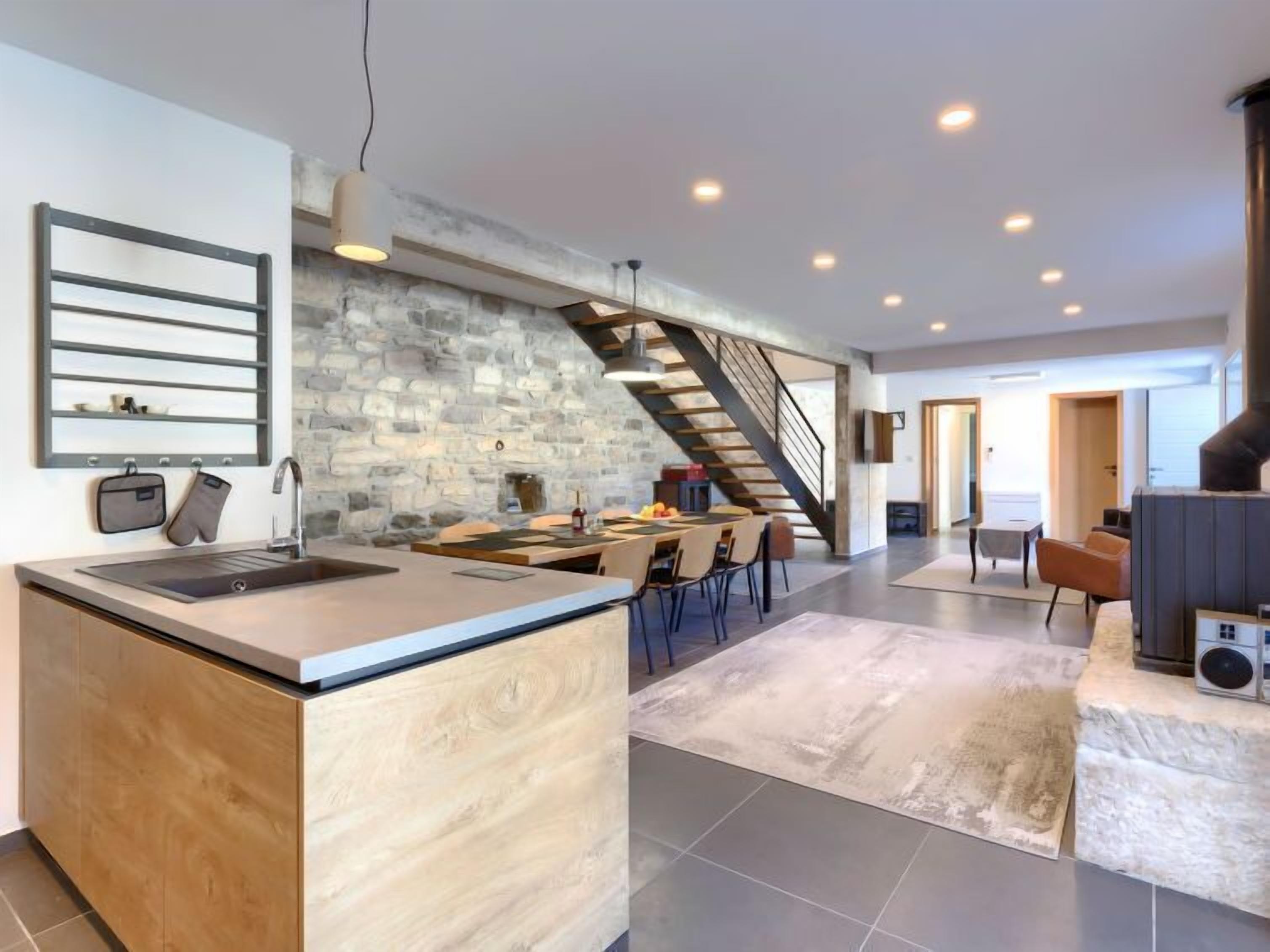 A modern kitchen with a stone wall, a central island, and a dining area with a staircase.
