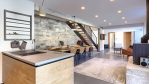 Une cuisine moderne avec un mur en pierre, un îlot central et un coin repas agrémenté d’un escalier.