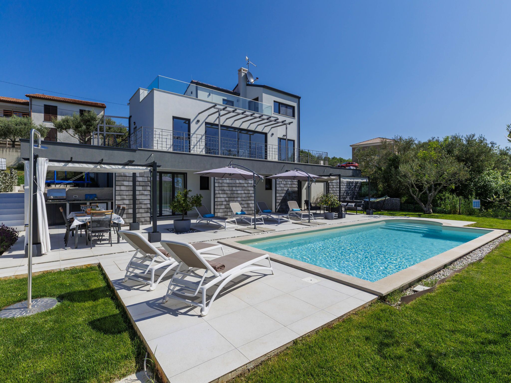 Et moderne hus i to etager med swimmingpool, udendørs siddeplads og grillområde.