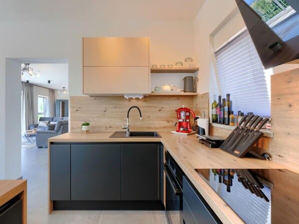 Une cuisine moderne dotée d’un îlot central, de meubles de couleur noire, d’un évier en acier inoxydable et d’un meuble à vin.