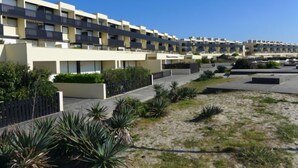 Un moderno complejo de apartamentos con varios balcones, un jardín ajardinado y un cielo azul despejado.