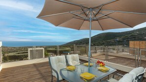 Un tavolo da pranzo con sedie e un ombrellone su un molo in legno con vista panoramica.