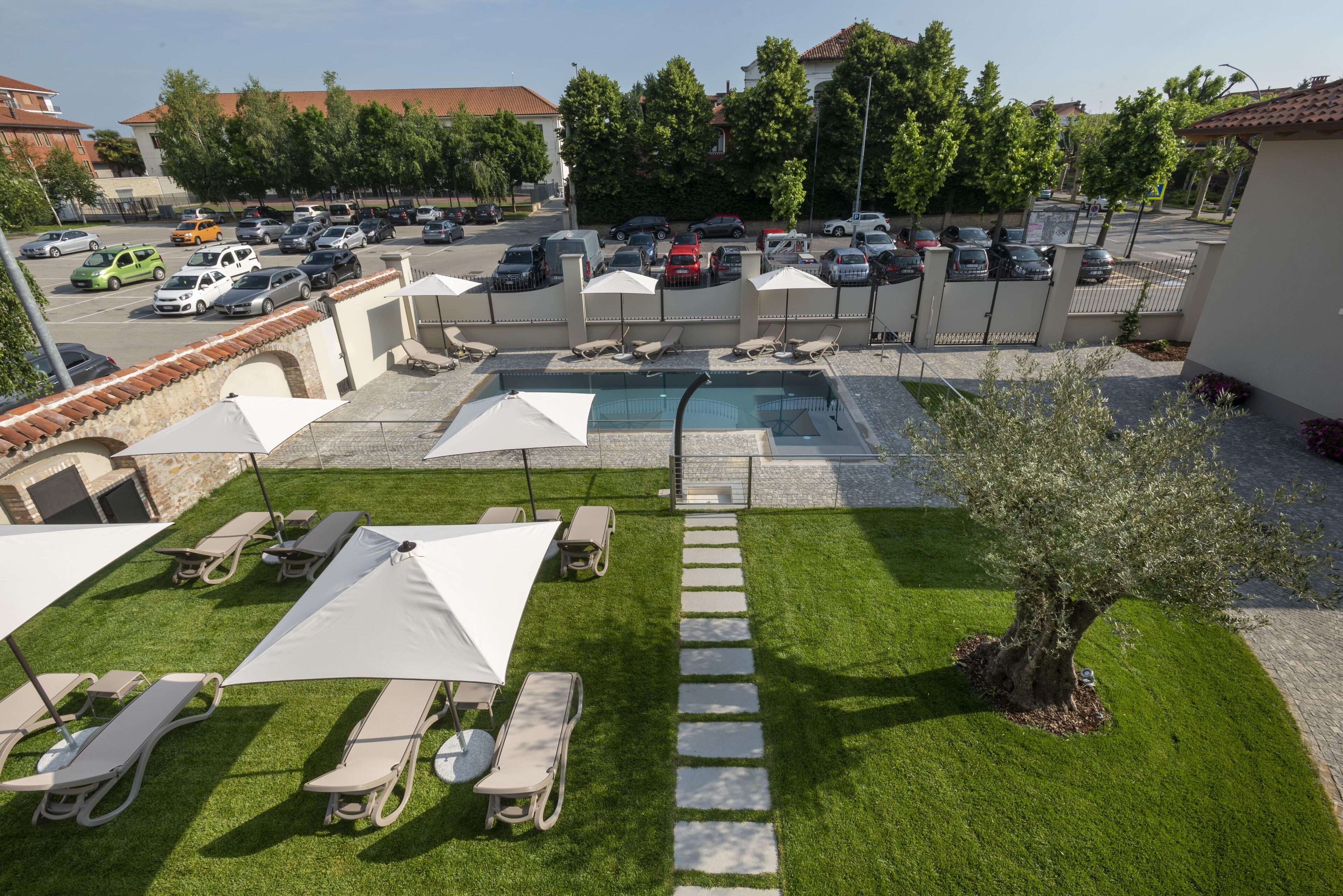 A hotel courtyard with a swimming pool, lounge chairs, umbrellas, and a parking lot.