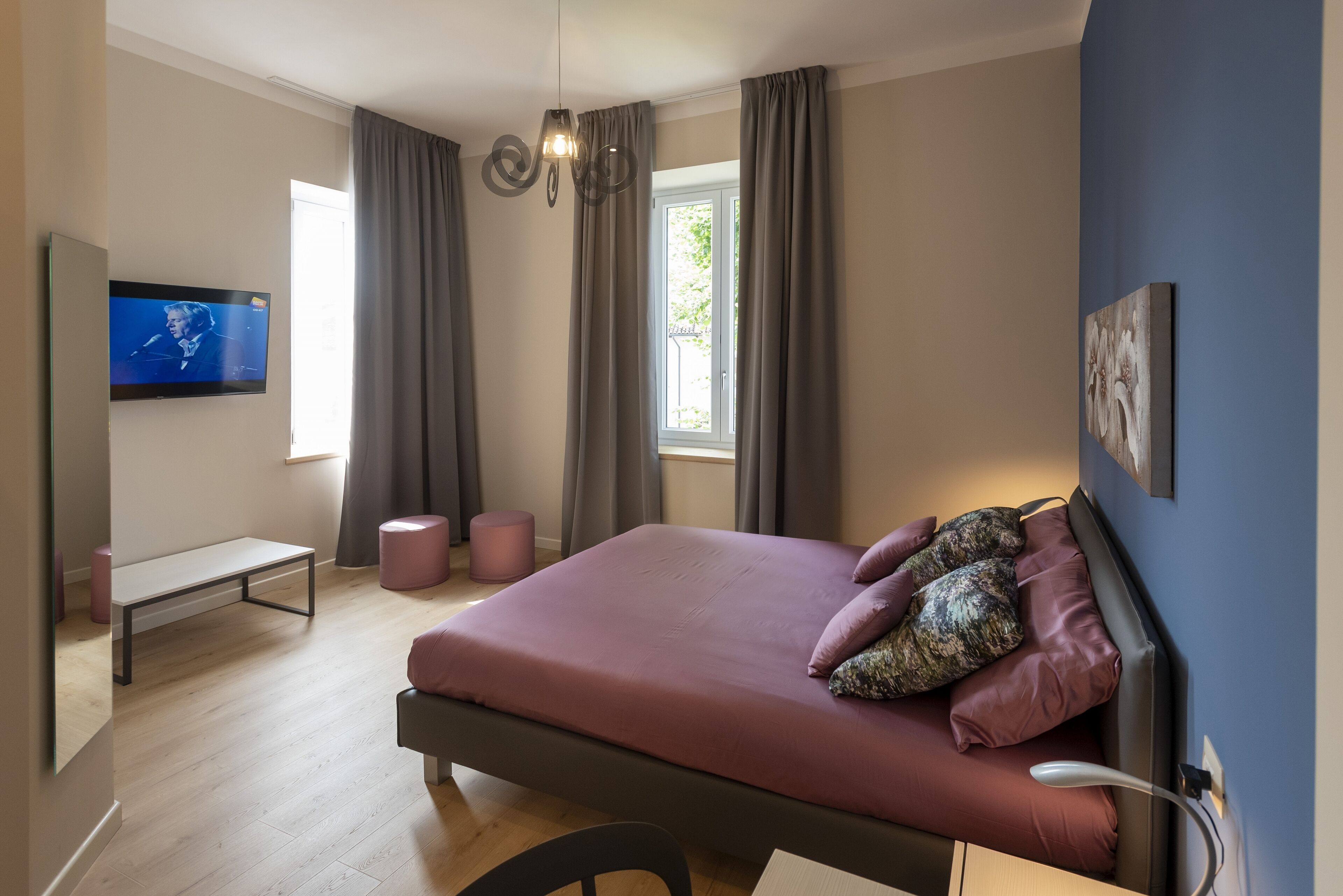 A bedroom with a bed, a bench, a TV, and a window.