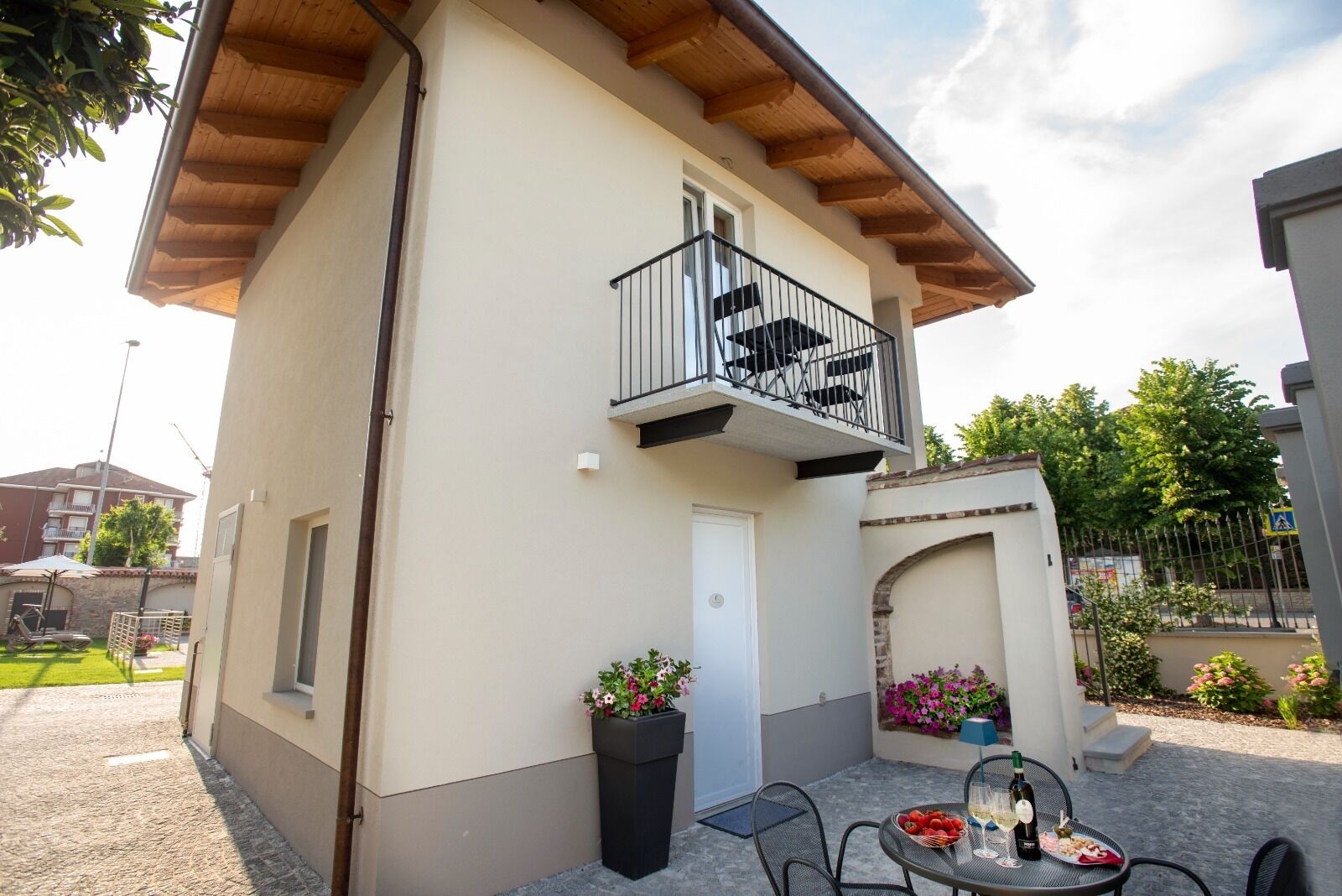 A two-story building with a balcony, a small outdoor seating area with a table and chairs, and potted plants.
