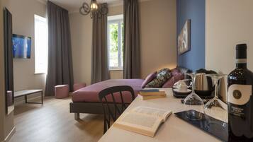 A modern hotel room with a bed, a desk with books and wine glasses, a bench, and a TV.