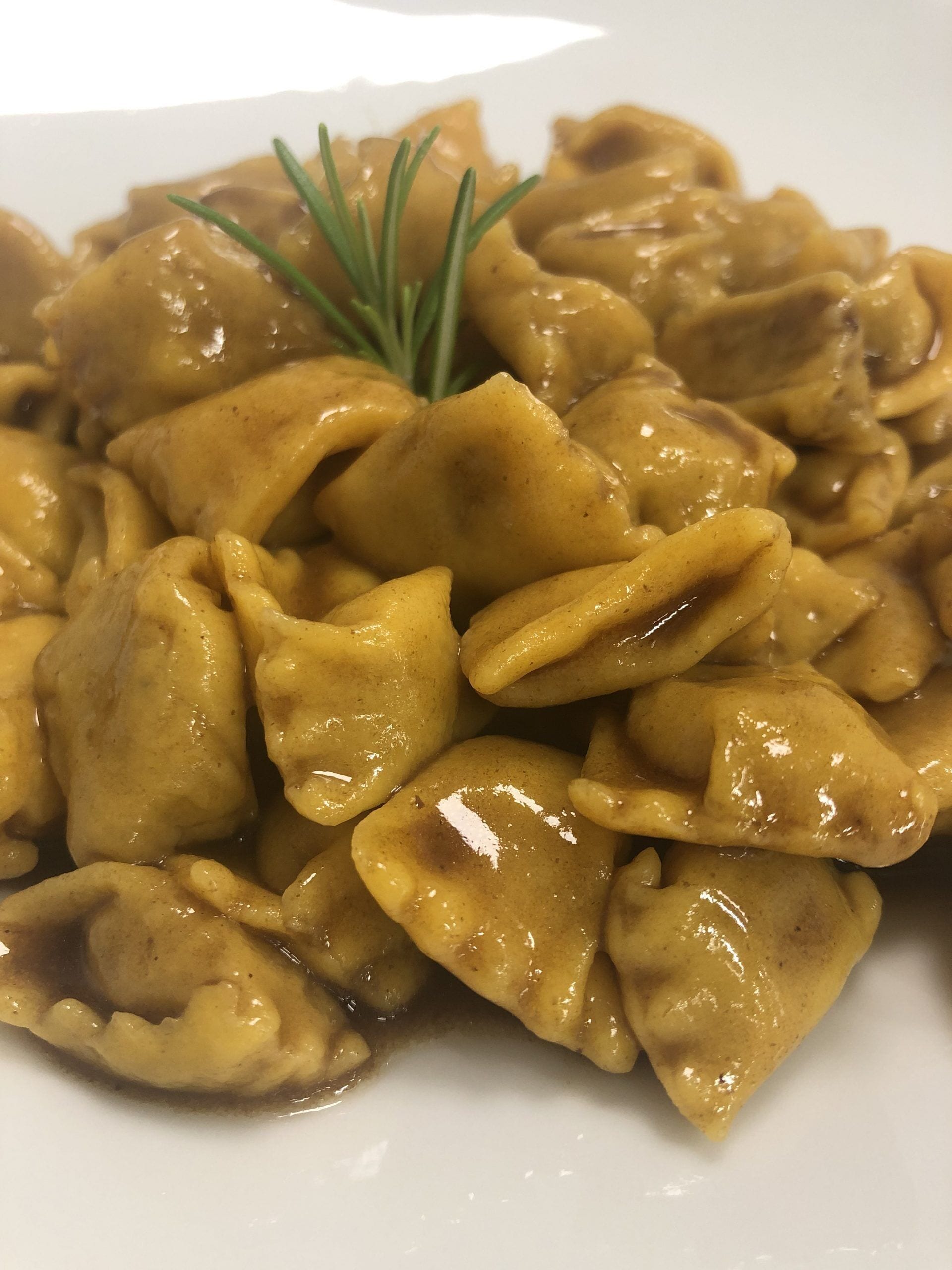 A plate of ravioli with a creamy sauce and a sprig of rosemary.