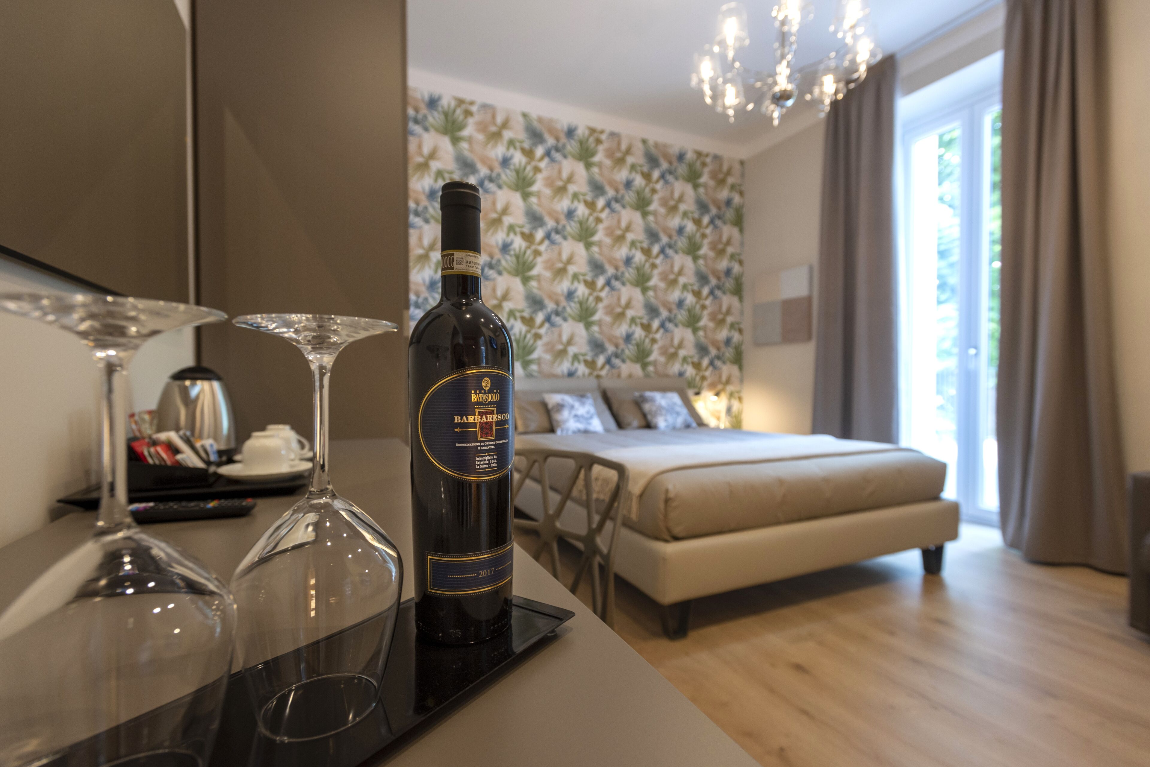 Een hotelkamer met een bed, een eettafel en twee wijnglazen op een dienblad.
