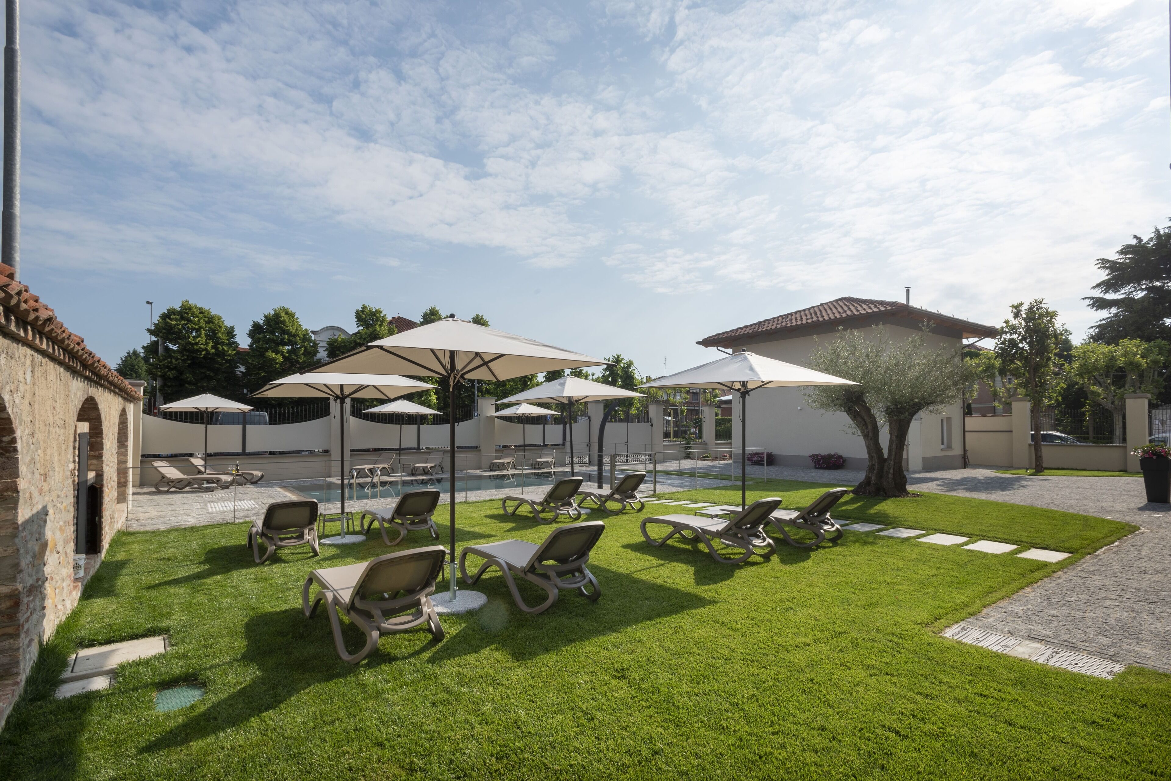 Ein Poolbereich mit Liegestühlen und Sonnenschirmen, einer gepflegten Rasenfläche und einer Steinmauer.