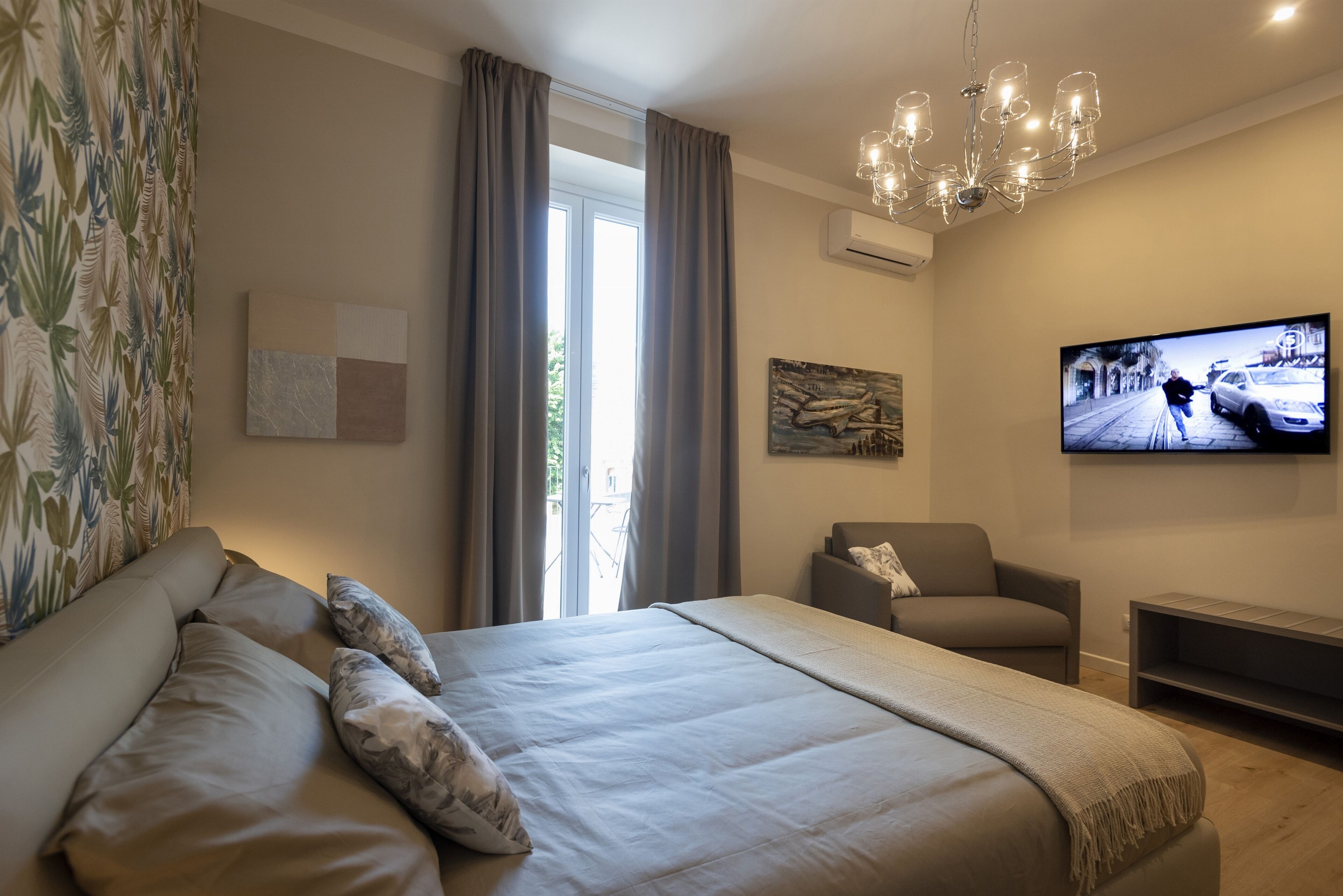 Une chambre moderne avec un grand lit, une télévision, un fauteuil et une fenêtre avec des rideaux.